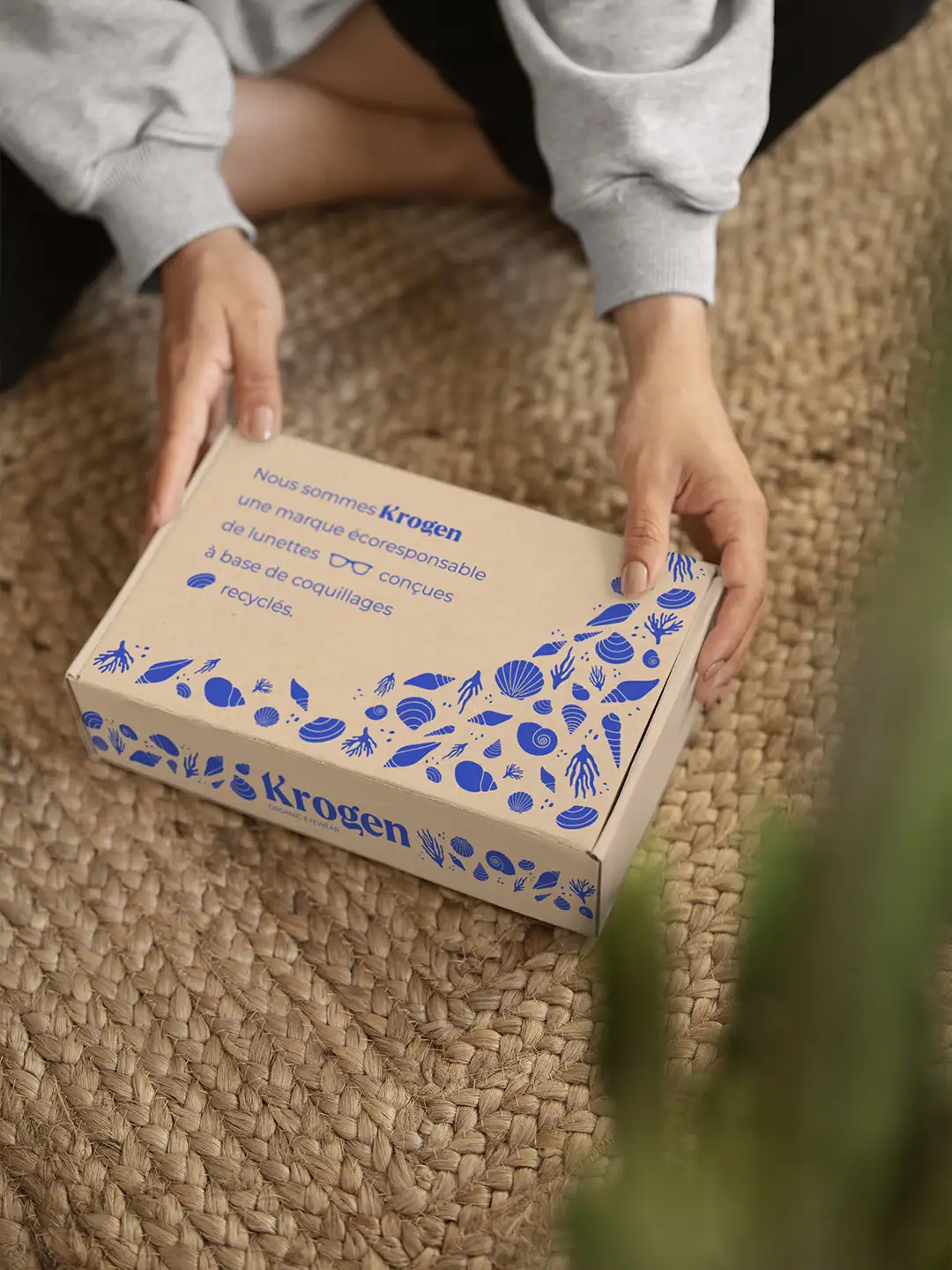 Boîte de packaging tenue en main avec l'identité visuelle de Krogen, marque de lunettes en coquillages recyclés